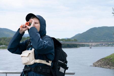 Man looking through a small telescope at a river landscape, demonstrating travel gear in real use during outdoor exploration.