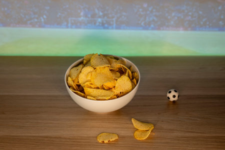 Bowl of potato chips on a table with a small soccer ball decoration, creating a football night atmosphere with comforting food.