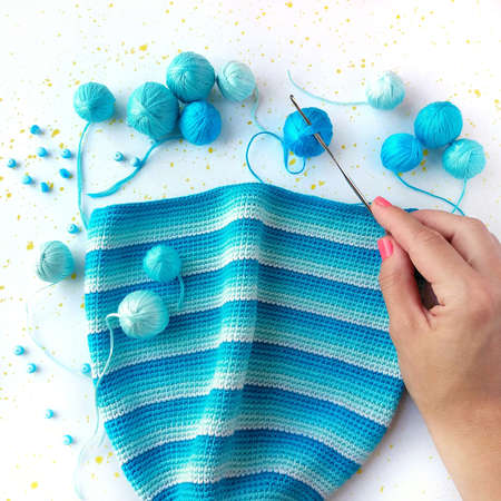 Crocheted hat with horizontal blue stripes, next to balls of blue yarn.の写真素材