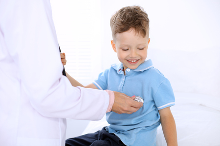 Happy little boy having fun while is being examine by doctor by stethoscope. Health care, insurance and help concept.の写真素材