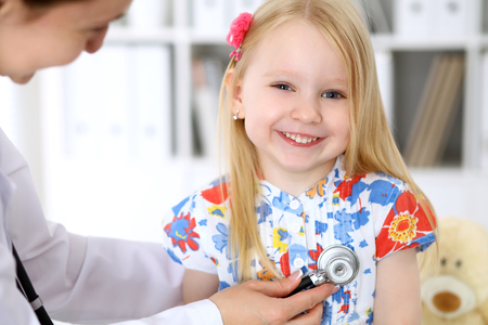 Pediatrician is taking care of baby in hospital. Little girl is being examine by doctor by stethoscope. Health care, insurance and help concept.の写真素材