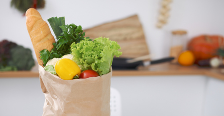 Paper bag full of vegetables on the table in kitchen interiors. Healthy meal and vegetarian concept.の写真素材