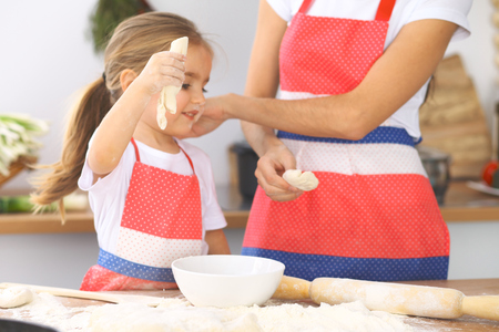 Mother and her cute daughter prepares the dough at wooden table. Homemade pastry for bread or pizza. Bakery backgroundの写真素材