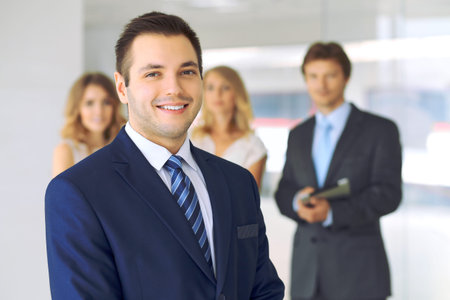 Smiling businessman in office with colleagues in the background