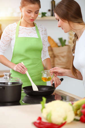 Two women friends choose the recipe and ingredients for a delicious meal in sunny kitchen. Vegetarian conceptの写真素材