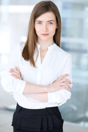 Beautiful female specialist with arms crossed standing in modern office and smiling charmingly. Working on design, data analysis, plan strategy. Business people conceptの写真素材