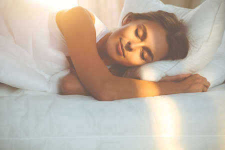 Beautiful blonde girl sleeping sweetly in sunny bedroom on a white bed. Holyday comfort and Rest conceptsの写真素材