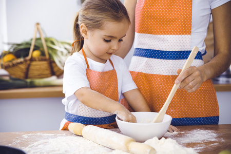 Happy woman and her daughter are kneading the dough and baking cookies for a delicious family...