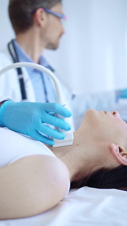 Doctor man wearing blue protective gloves is using ultrasound machine to examine neck of female...