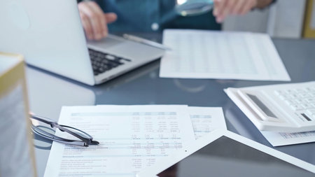 Close-up of a calculator with a male professional auditor working with spreadsheets and a laptop on...