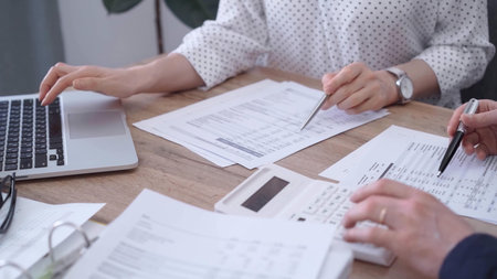 Bookkeeper woman is working with a colleague, using magnificent glass, calculator and laptop. Audit...