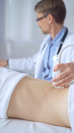 Doctor man is using ultrasound equipment on the back of a patient, woman. The results are on a...