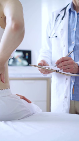 Doctor and patient. Physician is making notes on a clipboard while patient woman is describing...