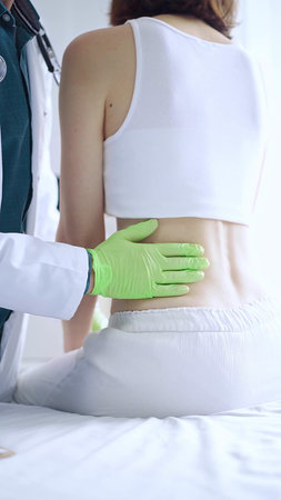 Doctor and patient. Physician wearing green medical gloves examining back of female patient in...