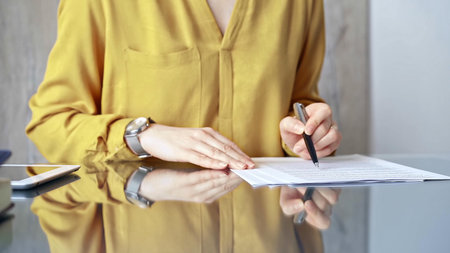 Businesswoman in yellow blues analyzing document at desk. Close-up of a professional auditor or lawyer reviewing a lengthy paper report in office setting. Business people conceptの写真素材