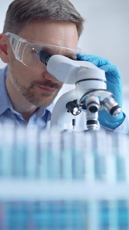 Man scientist with protective glasses and gloves is using microscope in laboratory, vertical...