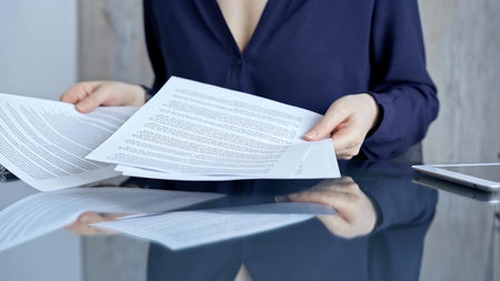 Businessperson woman in dark blue blouse analyzing document at glass desk. Close-up of a...