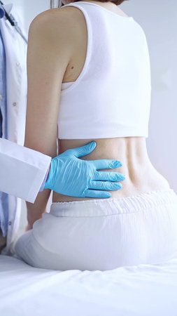 Doctor and patient. Physician wearing blue gloves examining back of female patient in clinic....