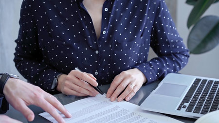 Detailed view of two business people or lawyers signing a contract with a laptop nearbyの写真素材