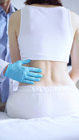 Doctor and patient. Physician wearing blue gloves examining back of female patient in clinic. Orthopedics in medicineの写真素材