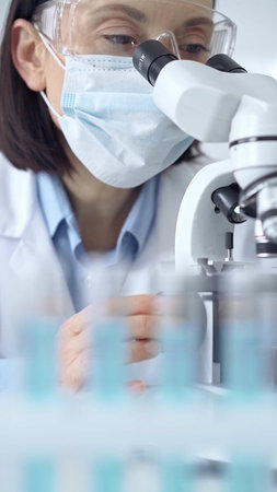 Female scientist using microscope in laboratory, portrait. Focus on a woman in lab goggles analyzing...