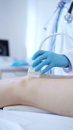 Male doctor with blue protective gloves using ultrasound machine on the knee of a female patient. Medicine conceptの写真素材