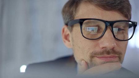 Businessman with glasses looking intently obscured partially by a translucent surface of laptop....