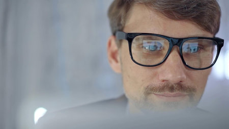 Businessman with glasses looking intently obscured partially by a translucent surface of laptop....
