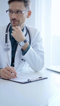 Doctor and a patient. The physician, wearing a white medical coat over a green shirt, gesturing with his hands during a consultation in the clinic. Medicine conceptの写真素材