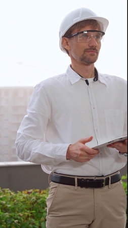 Male architect, wearing a white shirt and helmet, is using a digital tablet while inspecting a building site in foggy weather. Architecture and engineering conceptの写真素材