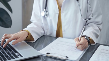Doctor woman is working on laptop with medical reports. Healthcare professional reviews patient files and inputs data in a clinic setting. Medicineの写真素材