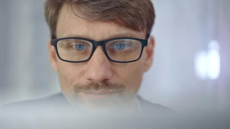 Businessman with glasses looking intently obscured partially by a translucent surface of laptop....