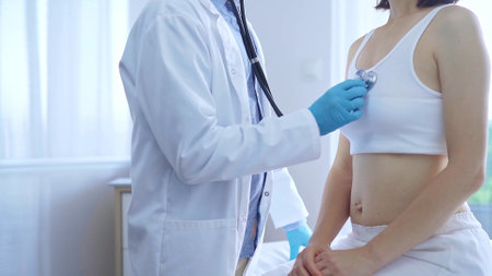 Doctor and patient. Physician wearing blue medical gloves is using stethoscope examining woman in clinic. Medicine conceptの写真素材