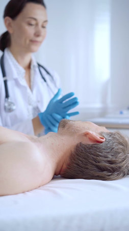 Doctor woman is putting on blue medical gloves and going to perform neck ultrasound exam on male patient. Medicine service conceptの写真素材