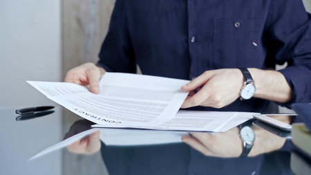Businessman in dark blue t-shirt analyzing document at desk. Close-up of a professional auditor or...