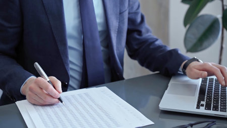 Businessman analyzing financial data on laptop and calculator. Close-up of a professional auditor working on financial reports. Business conceptの写真素材