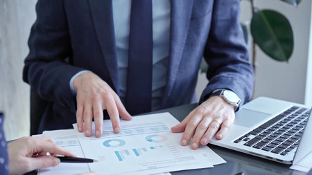 Professional businessman gestures to charts on laptop screen during corporate meeting. Business...