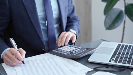 Businessman analyzing financial data on laptop and calculator. Close-up of a professional auditor working on financial reports. Business conceptの写真素材