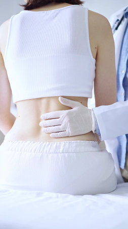 Doctor and patient. Physician wearing white medical gloves examining back of female patient in clinic. Orthopedics and pediatric in medicineの写真素材