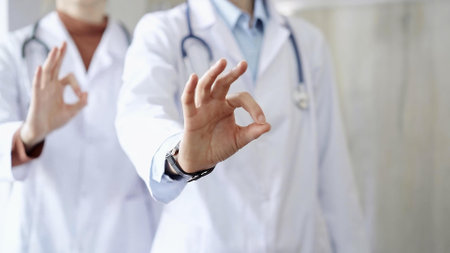 Two doctors is showing ok sign with fingers while standing in a hospital. Teamwork and success in medicineの写真素材