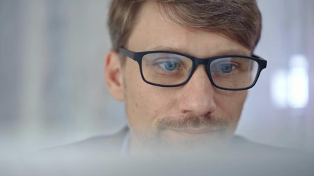 Businessman with glasses looking intently obscured partially by a translucent surface of laptop....
