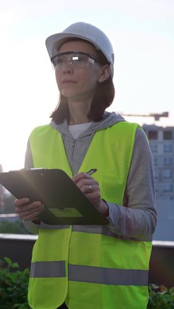 Woman a construction engineer is writing on a clipboard while inspecting a construction site in the early morning at sunrise, front viewの写真素材