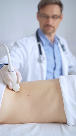 Doctor man wearing white protective gloves is using ultrasound equipment on the back of a patient, woman. The results are on a monitor in the background. Medicine serviceの写真素材