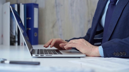 Businessman with blue suit is working on his laptop, typing on the keyboard in the office. Business...