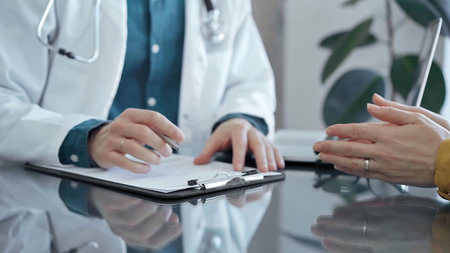 Doctor and patient consultation in clinic. Physician making notes while senior women is gesturing...