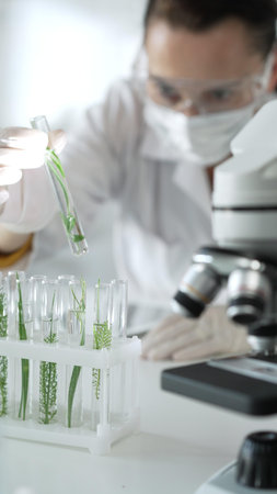 Woman scientist with white gloves, face mask and protective glasses, is holding a test tube with...