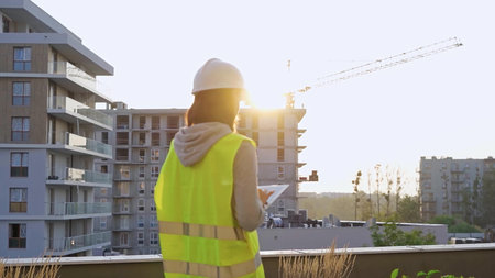 Construction female engineer taking notes and tapping on tablet computer while inspecting a building...