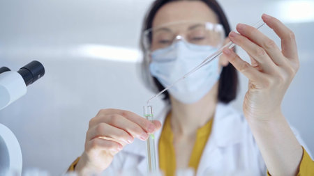 Woman with safety glasses and blue mask is working with lab tubes using a pipette in a modern laboratory, close-up of researcher. Science and medicineの写真素材