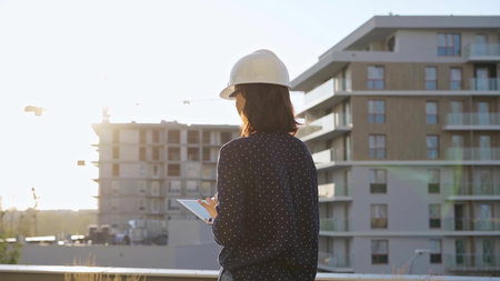 Female architect wearing a safety helmet is using a tablet computer while inspecting a building...