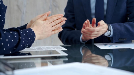 Unrecognizable business people shaking hands and clapping over glass table after contract signing in...